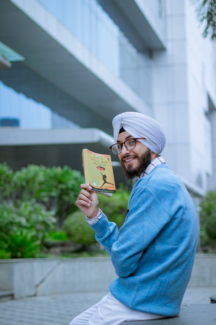 Happy man in glasses with turban holding a book outdoors.